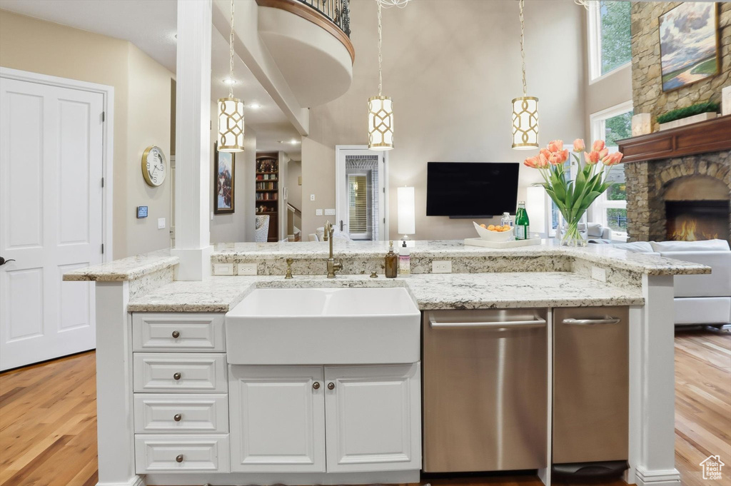 Kitchen featuring light wood finished floors, open floor plan, pendant lighting, stainless steel dishwasher, and white cabinets