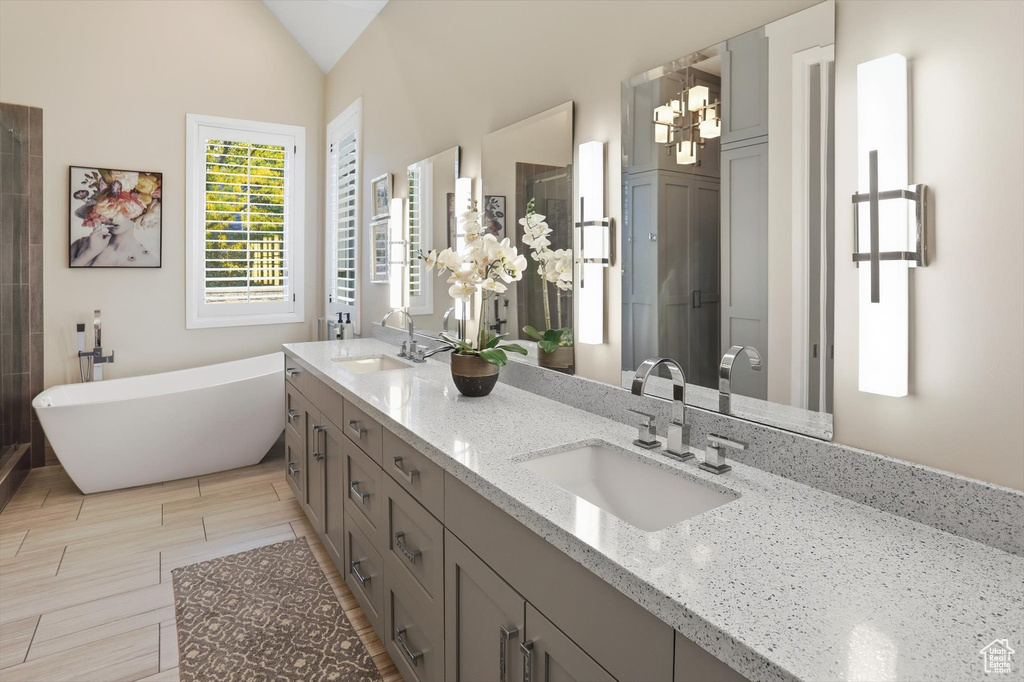 Bathroom with double vanity, a freestanding tub, a stall shower, light wood-style flooring, and a chandelier