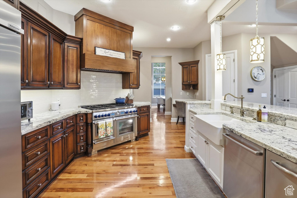 Kitchen with premium appliances, tasteful backsplash, pendant lighting, light stone counters, and light wood-style floors