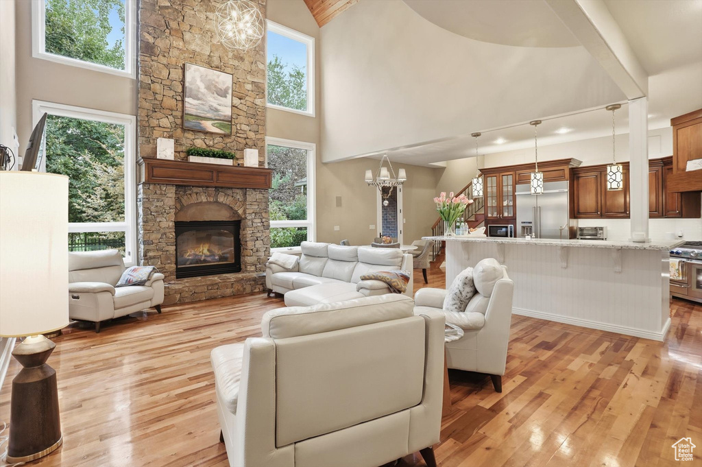 Living area featuring light wood-style floors, a chandelier, healthy amount of natural light, a fireplace, and high vaulted ceiling