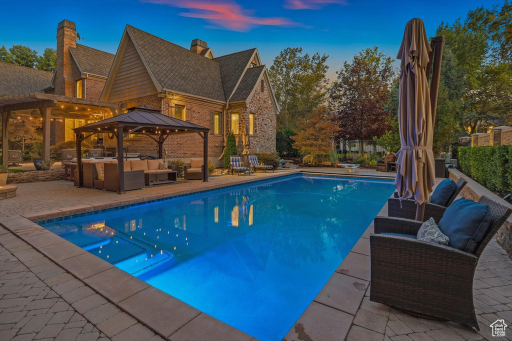 Pool at dusk with an outdoor living space, a gazebo, and a patio