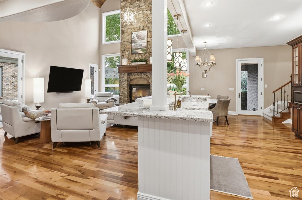 Living room with a stone fireplace, healthy amount of natural light, stairs, light wood-type flooring, and high vaulted ceiling