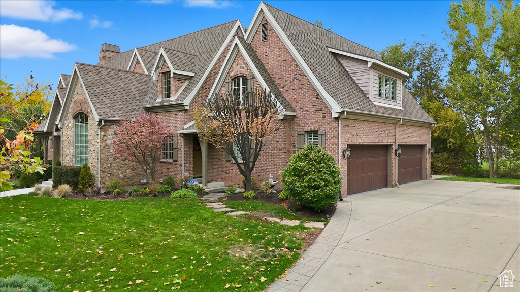 View of front of property with brick siding, a front yard, concrete driveway, roof with shingles, and a chimney