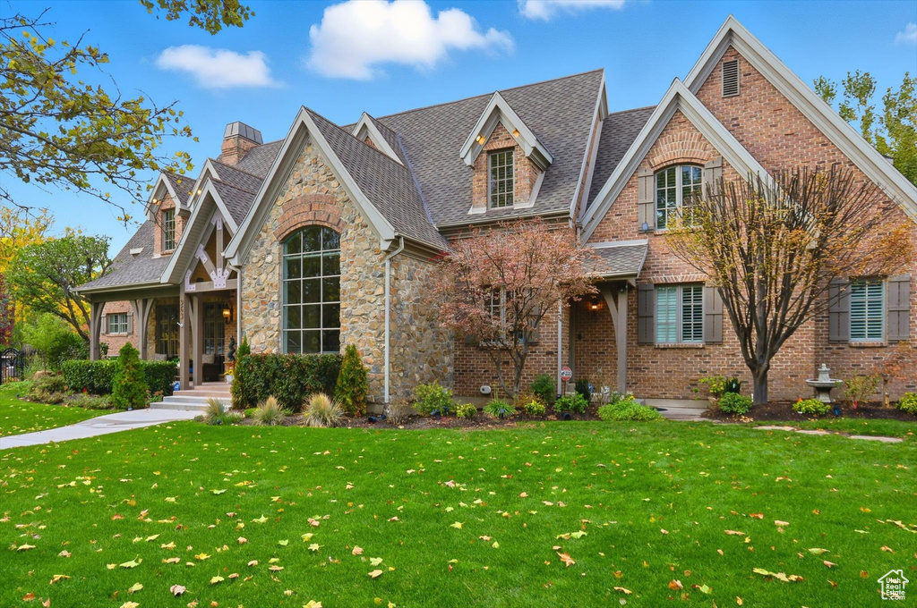 Tudor home featuring a front yard, a chimney, stone siding, brick siding, and roof with shingles