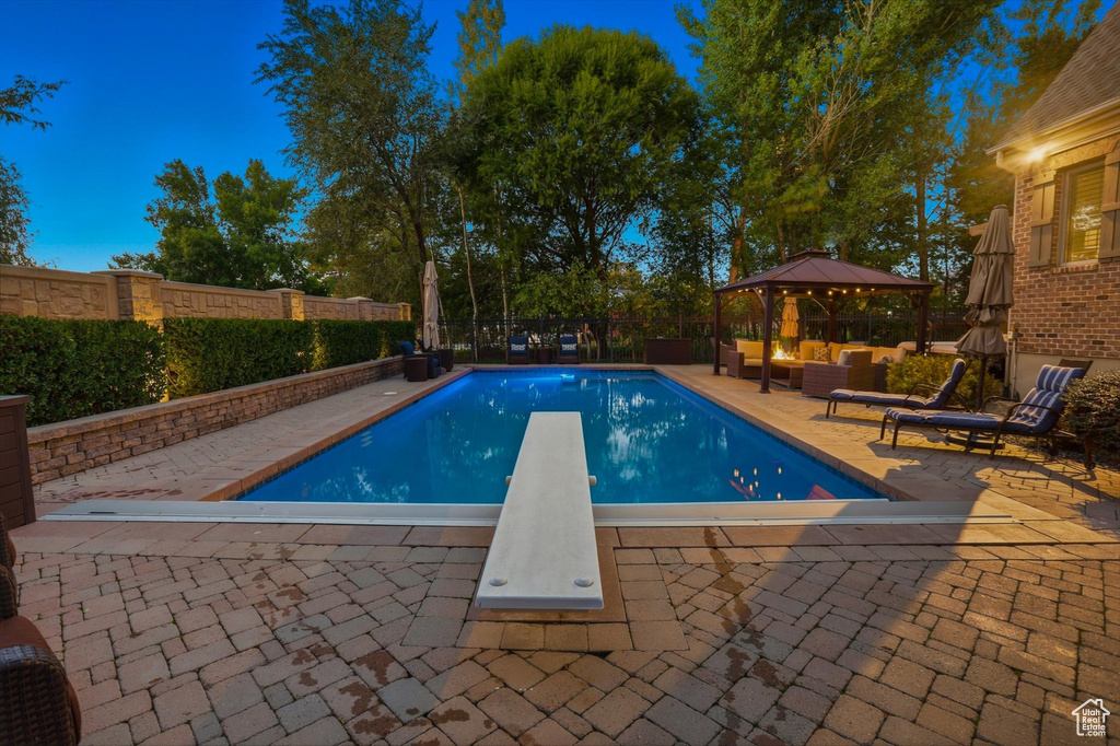 View of pool featuring a diving board, a gazebo, a patio area, a fenced backyard, and an outdoor living space