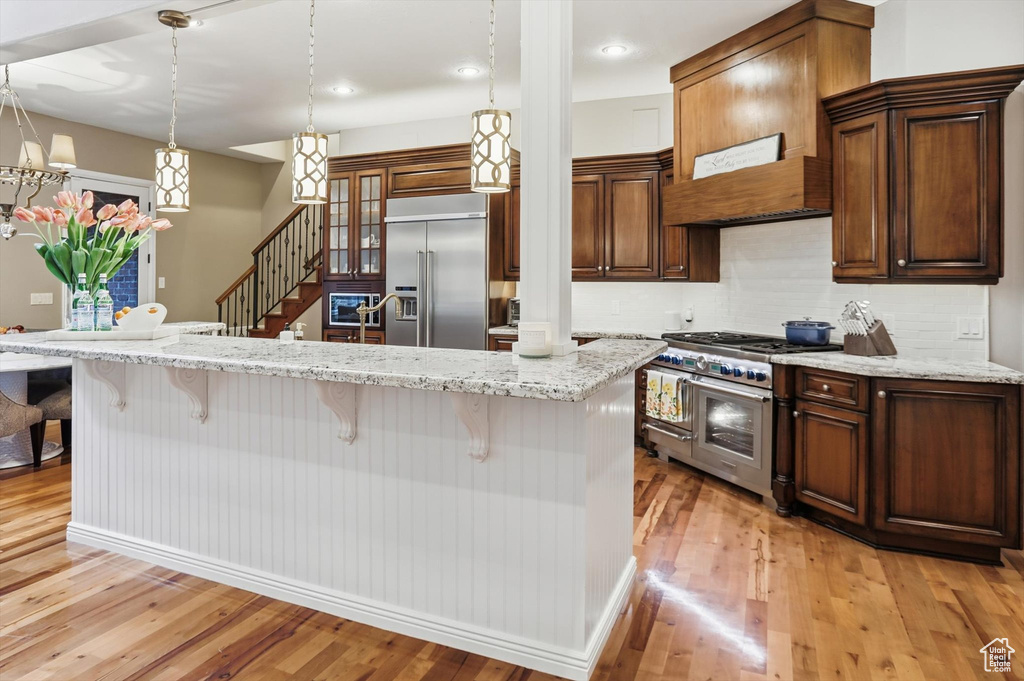 Kitchen with decorative backsplash, light stone counters, high end appliances, pendant lighting, and a breakfast bar area