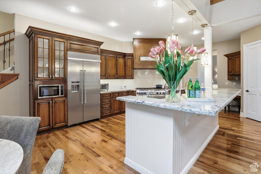 Kitchen featuring built in appliances, light wood-type flooring, light stone countertops, a breakfast bar area, and recessed lighting