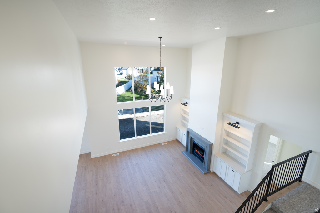 Unfurnished living room featuring recessed lighting, light wood-type flooring, a lit fireplace, a chandelier, and a high ceiling