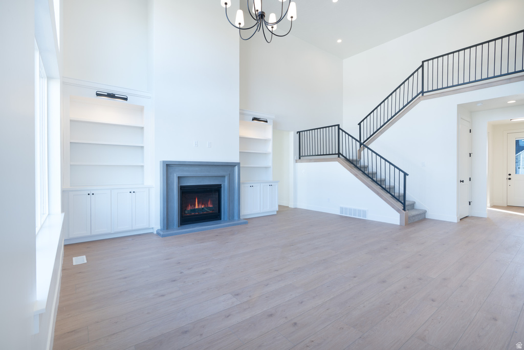 Unfurnished living room featuring a high ceiling, light wood-style flooring, a warm lit fireplace, a chandelier, and stairs