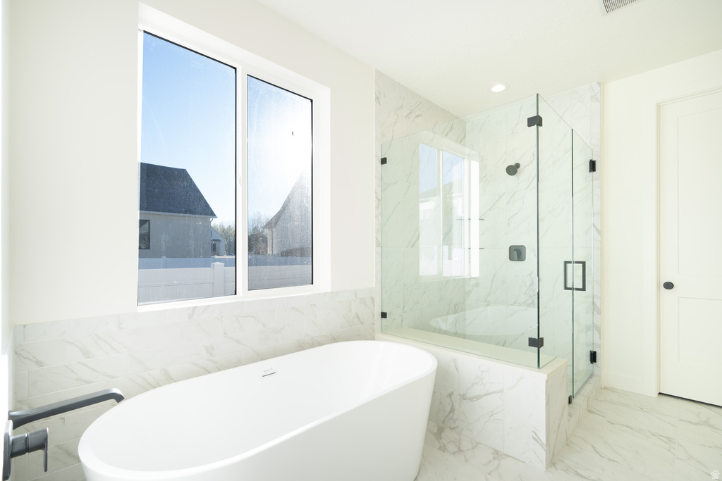 Bathroom featuring a soaking tub, healthy amount of natural light, marble tiled flooring, a marble finish shower, and tile walls
