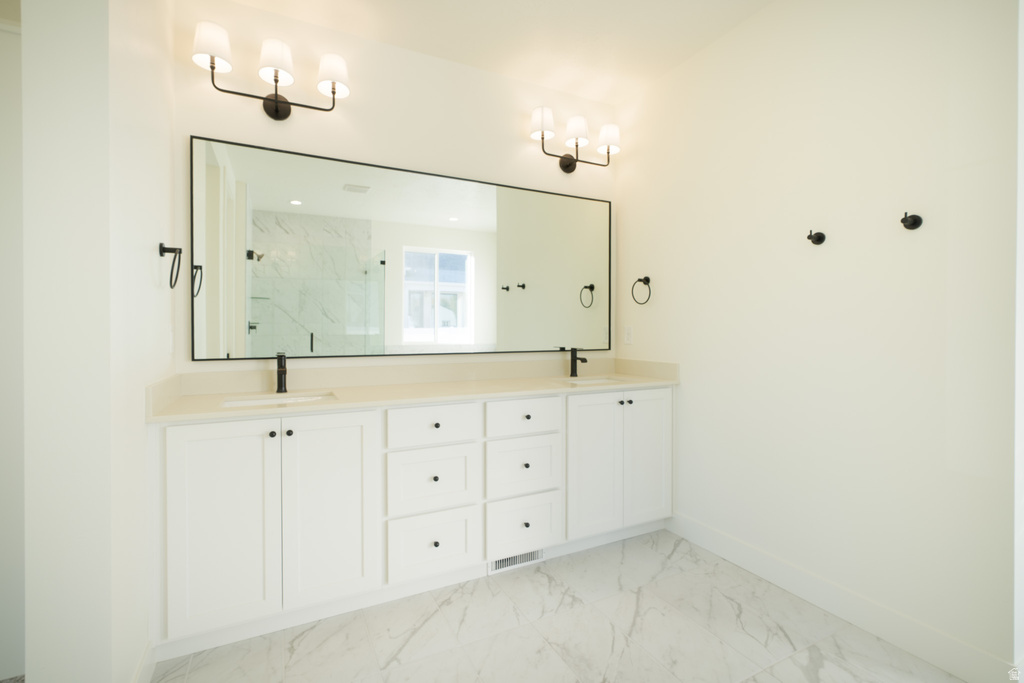 Bathroom featuring a marble finish shower, double vanity, and light marble finish floors