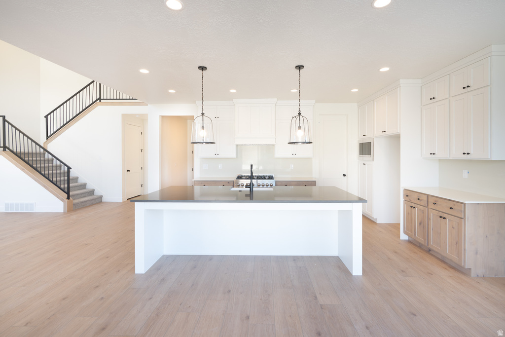 Kitchen featuring a large island, white cabinets, recessed lighting, light wood-style flooring, and decorative light fixtures