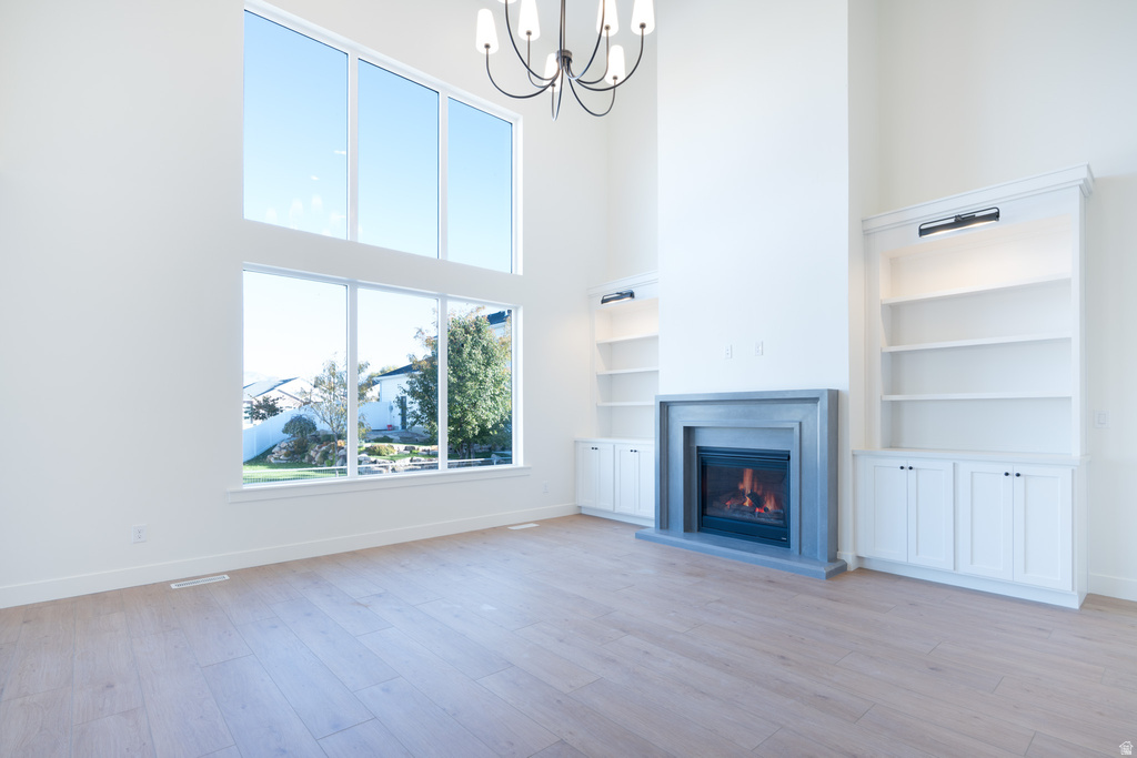 Unfurnished living room featuring a towering ceiling, a chandelier, light wood finished floors, a glass covered fireplace, and built in features