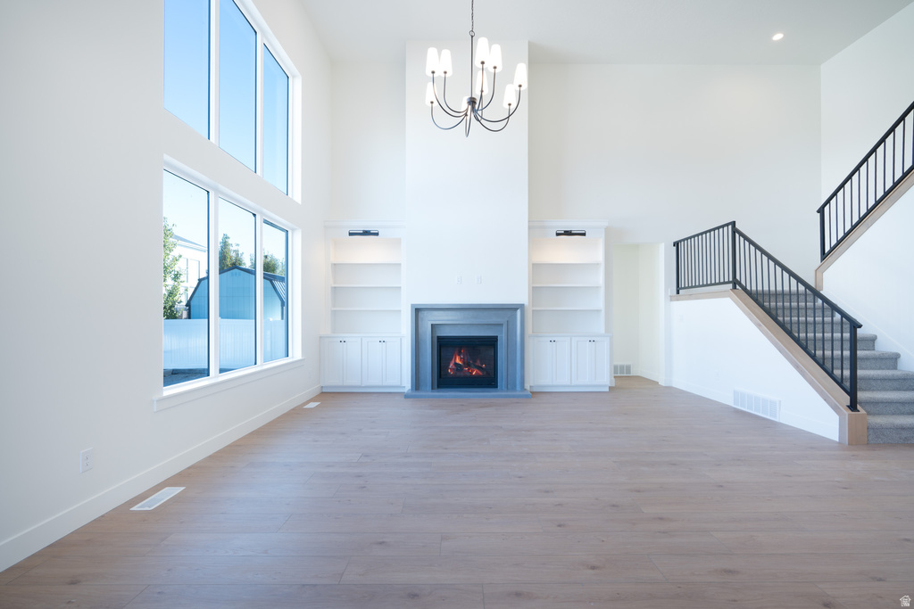 Unfurnished living room with a towering ceiling, a warm lit fireplace, light wood-style flooring, a chandelier, and stairway