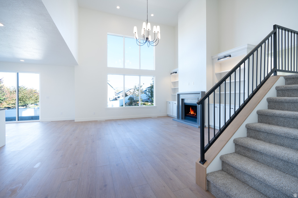 Unfurnished living room featuring stairway, light wood-style flooring, a warm lit fireplace, a high ceiling, and a chandelier