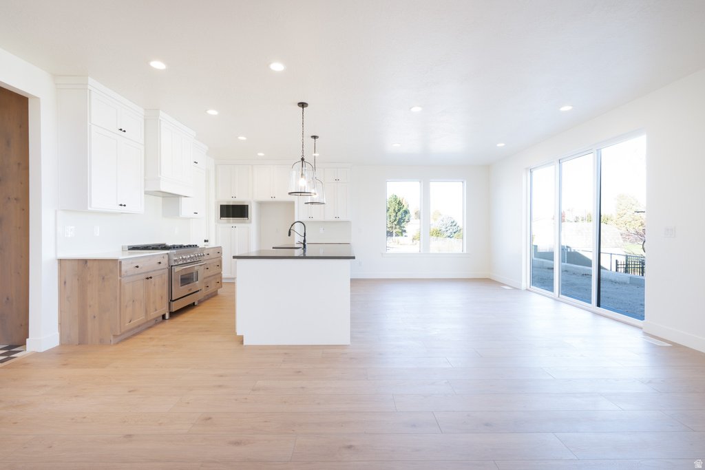 Kitchen featuring white cabinets, dark countertops, appliances with stainless steel finishes, decorative light fixtures, and recessed lighting