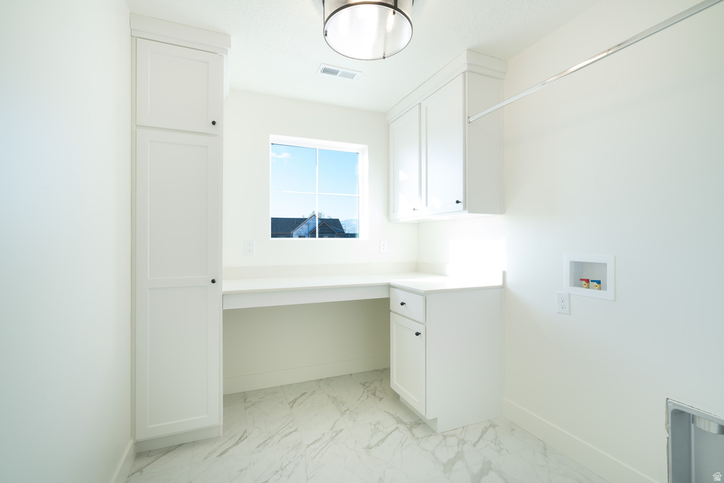 Washroom with hookup for a washing machine, light marble finish floors, a desk, and cabinet space