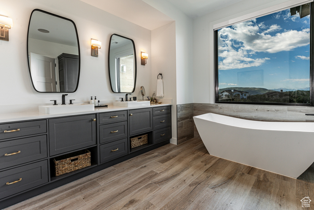 Bathroom with tile walls, double vanity, a freestanding bath, light wood-style flooring, and wainscoting