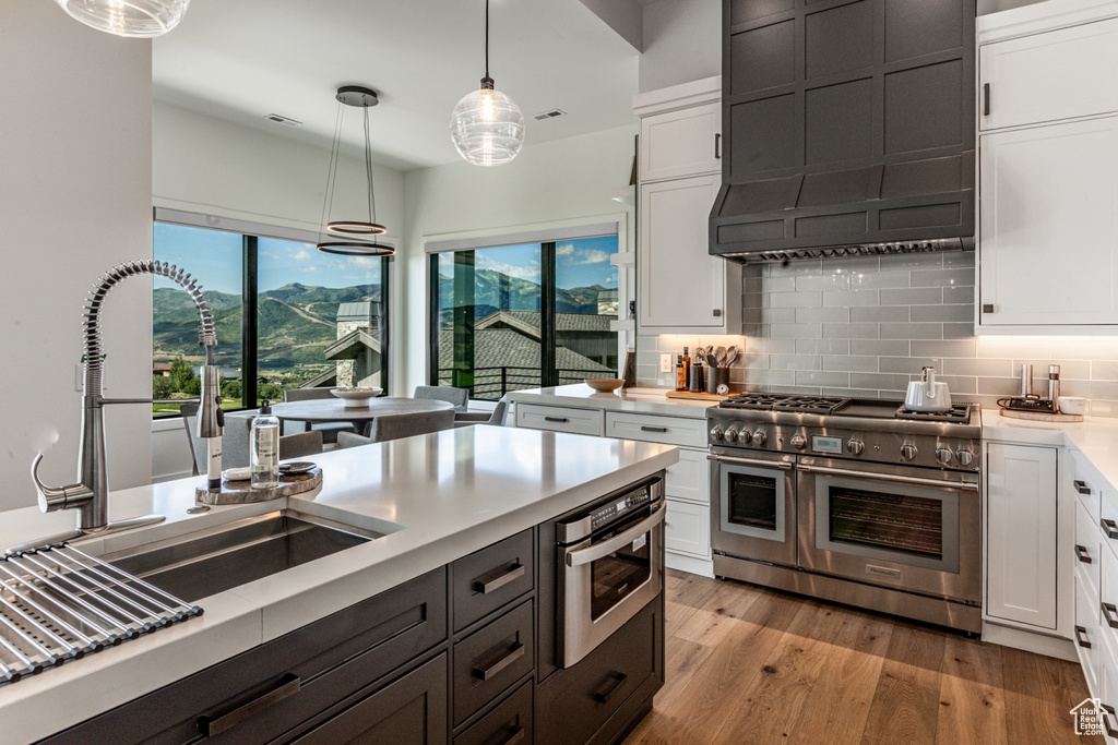 Kitchen featuring stainless steel appliances, white cabinets, light wood-style flooring, decorative light fixtures, and decorative backsplash