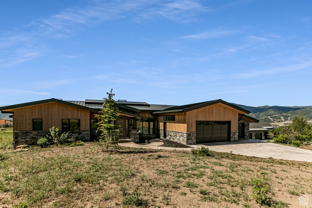 View of front of property featuring stone siding, driveway, solar panels, a standing seam roof, and an attached garage