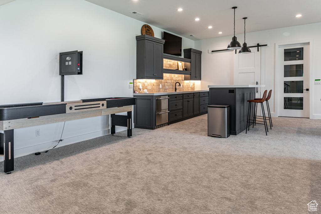 Kitchen featuring a barn door, backsplash, light countertops, a breakfast bar, and light carpet