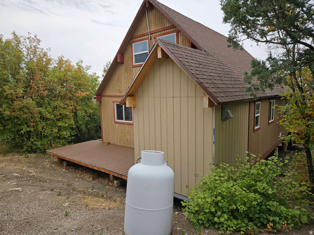 View of side of property with a shingled roof and a deck
