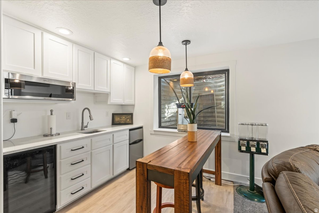 Kitchen featuring wine cooler, white cabinetry, light wood-type flooring, appliances with stainless steel finishes, and decorative light fixtures