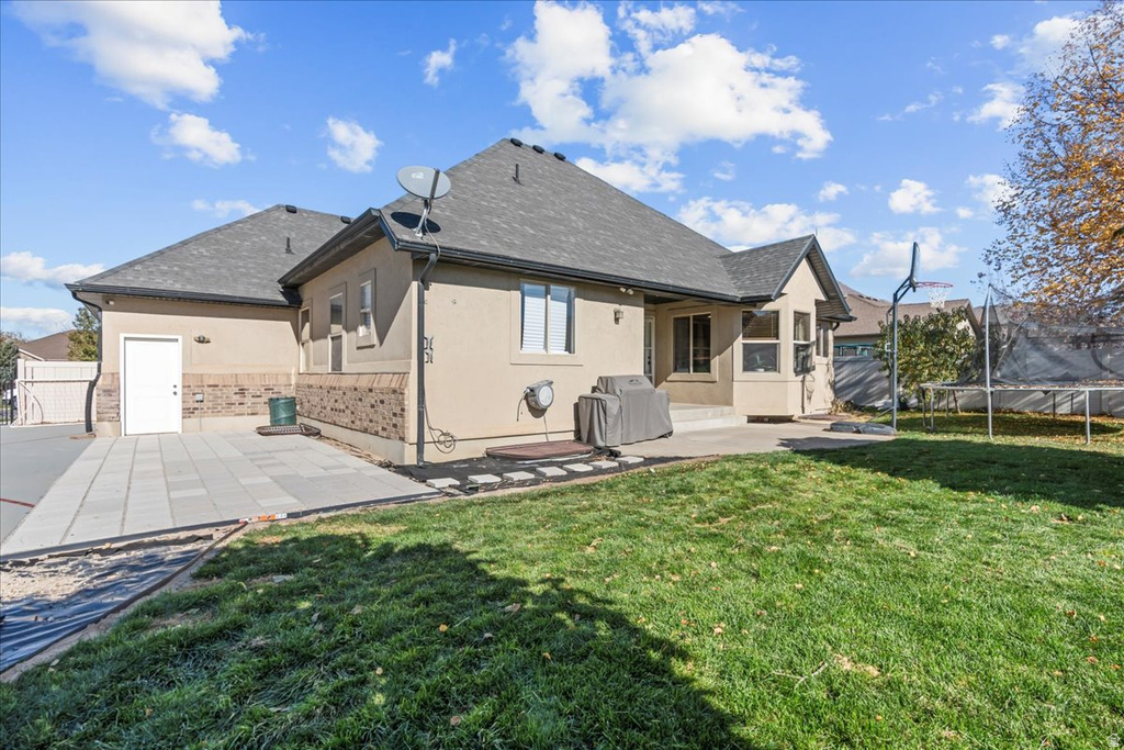 Rear view of house with a trampoline, a patio, stucco siding, and a gate