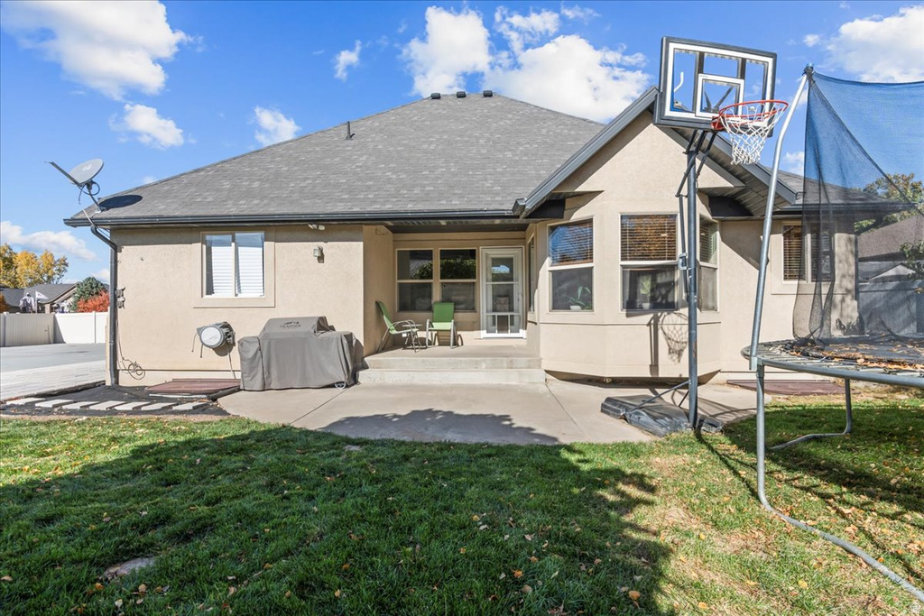 Back of house with a trampoline, a patio, stucco siding, and a shingled roof