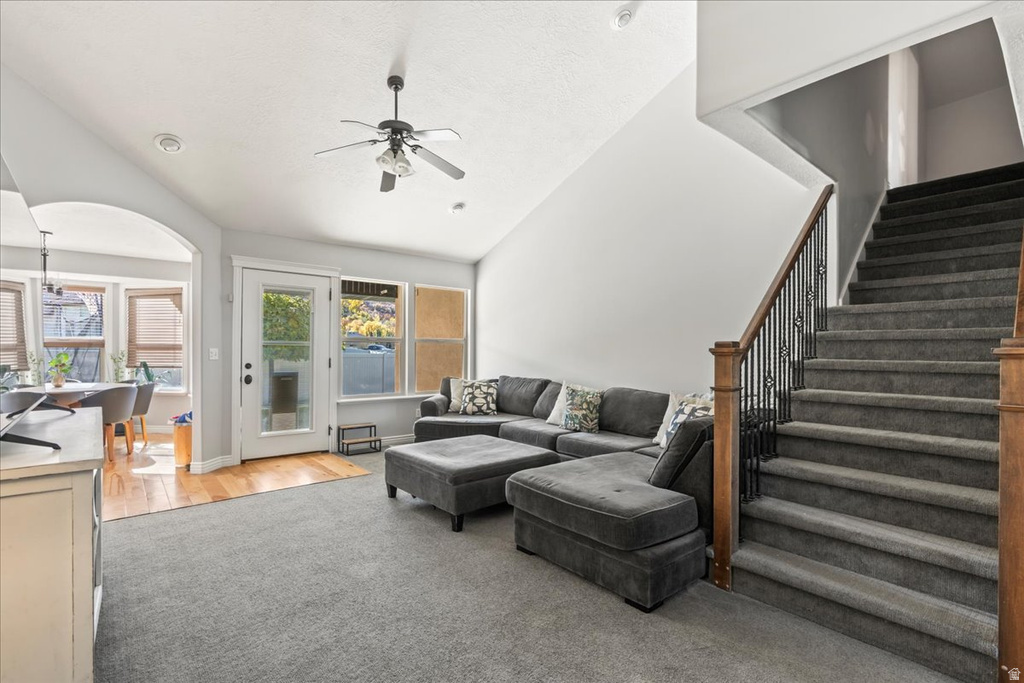 Living room featuring arched walkways, a ceiling fan, stairway, lofted ceiling, and light wood finished floors
