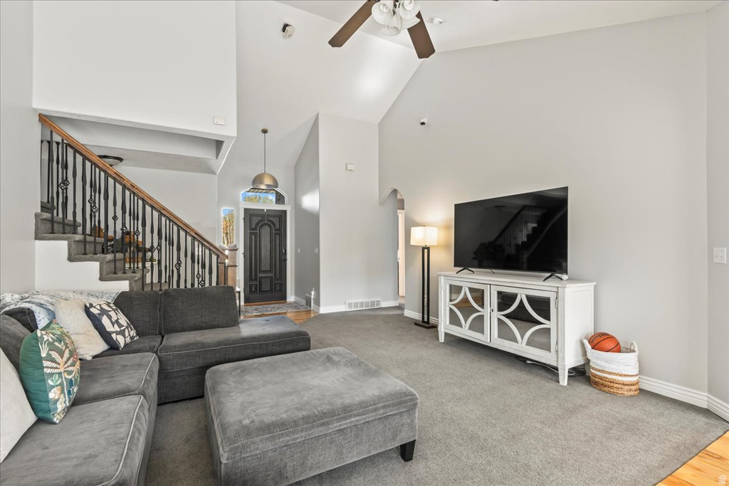 Carpeted living area featuring high vaulted ceiling, a ceiling fan, and stairs