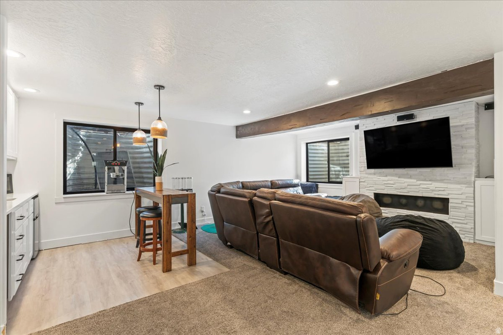 Living area with a textured ceiling, a stone fireplace, light colored carpet, recessed lighting, and light wood-style flooring