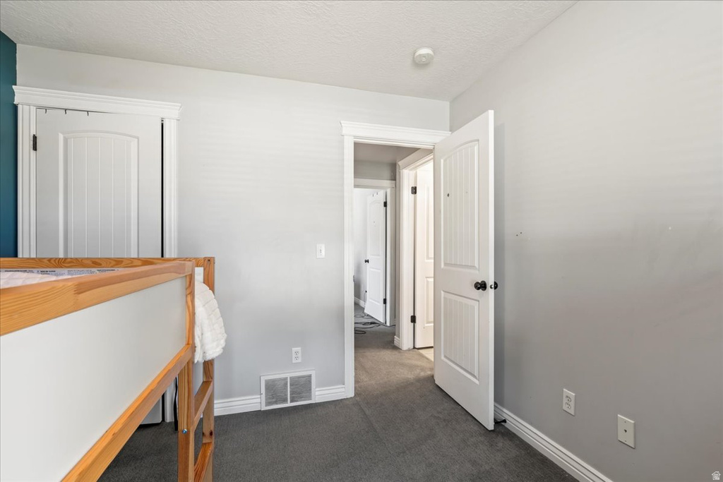Unfurnished bedroom featuring a textured ceiling and dark colored carpet