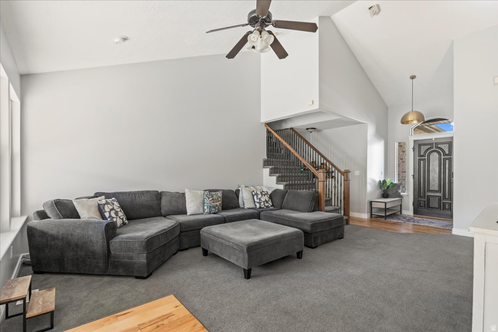 Living room with high vaulted ceiling, stairs, wood finished floors, ceiling fan, and carpet floors