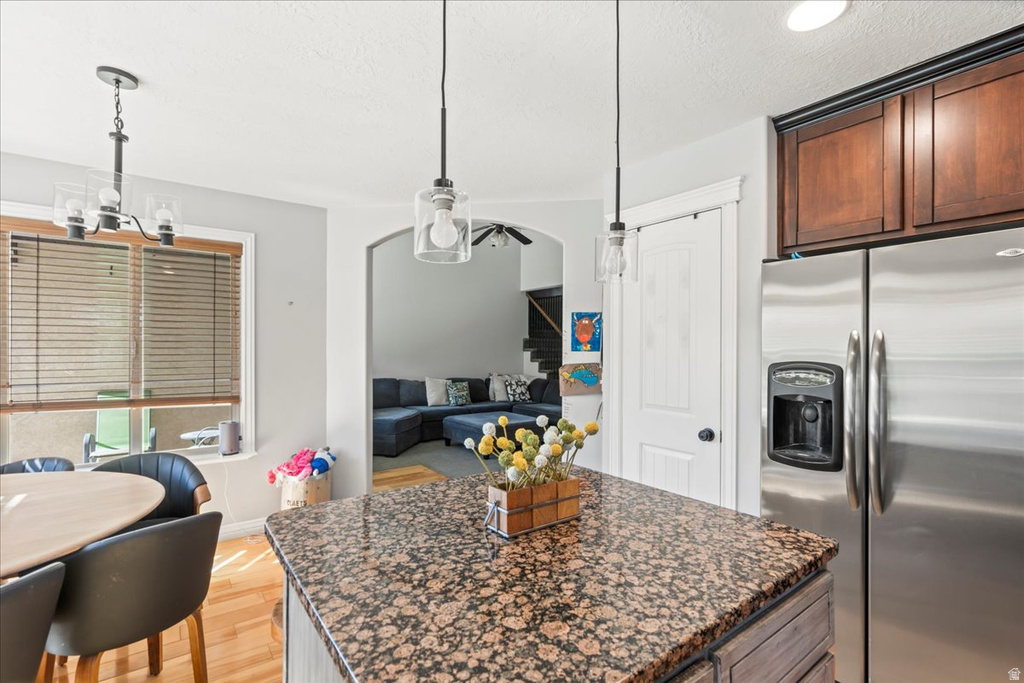 Kitchen with stainless steel fridge, dark stone counters, light wood-style floors, pendant lighting, and a kitchen island