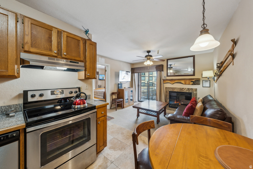 Kitchen with appliances with stainless steel finishes, a fireplace, hanging light fixtures, under cabinet range hood, and brown cabinetry