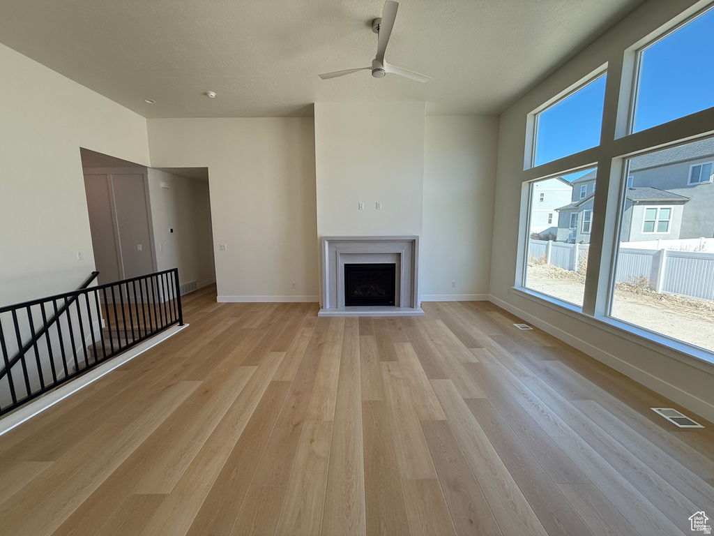 Unfurnished living room featuring light wood-type flooring, a ceiling fan, and a fireplace with raised hearth