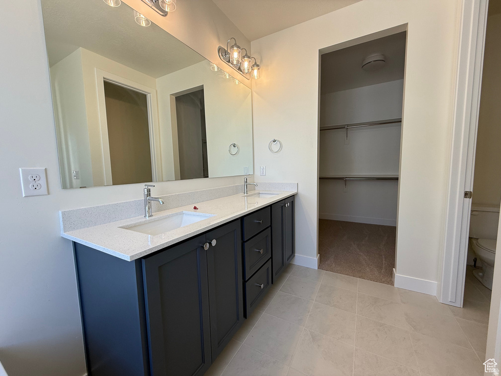 Bathroom with light tile patterned floors, double vanity, and a walk in closet