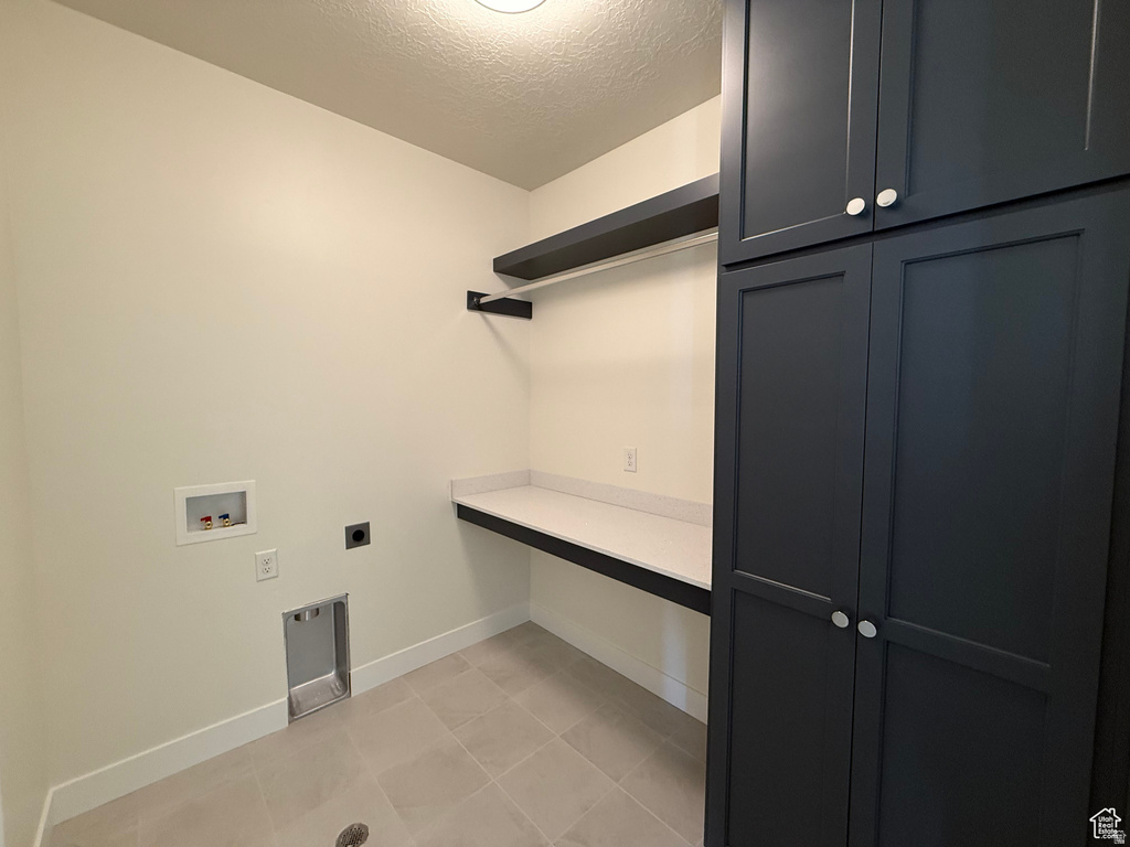 Laundry area with a textured ceiling, electric dryer hookup, washer hookup, and light tile patterned flooring