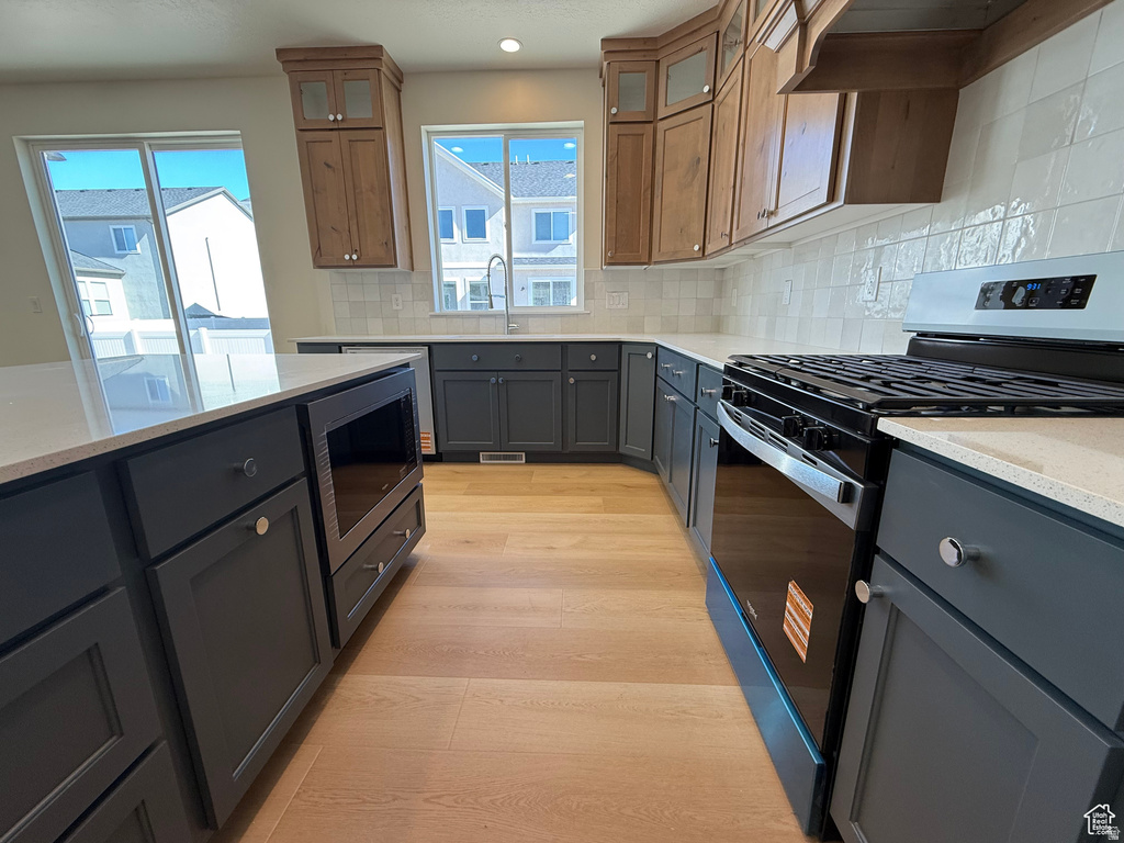 Kitchen featuring range with gas cooktop, tasteful backsplash, light stone counters, glass insert cabinets, and recessed lighting