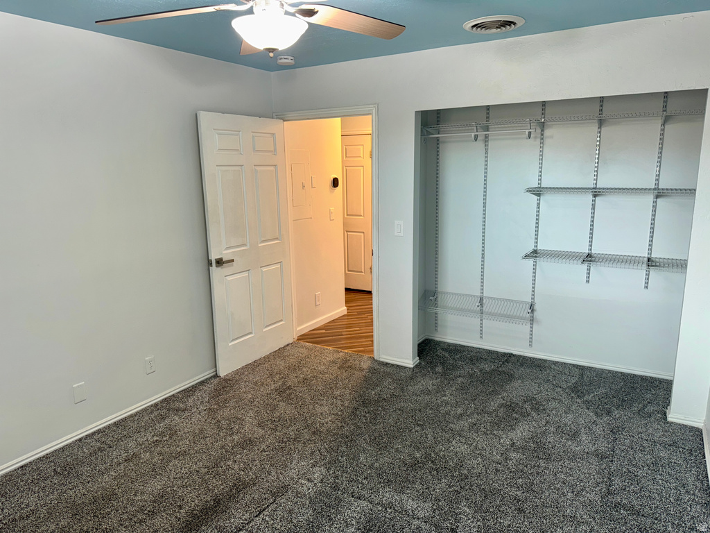 Unfurnished bedroom featuring dark carpet, a closet, and a ceiling fan