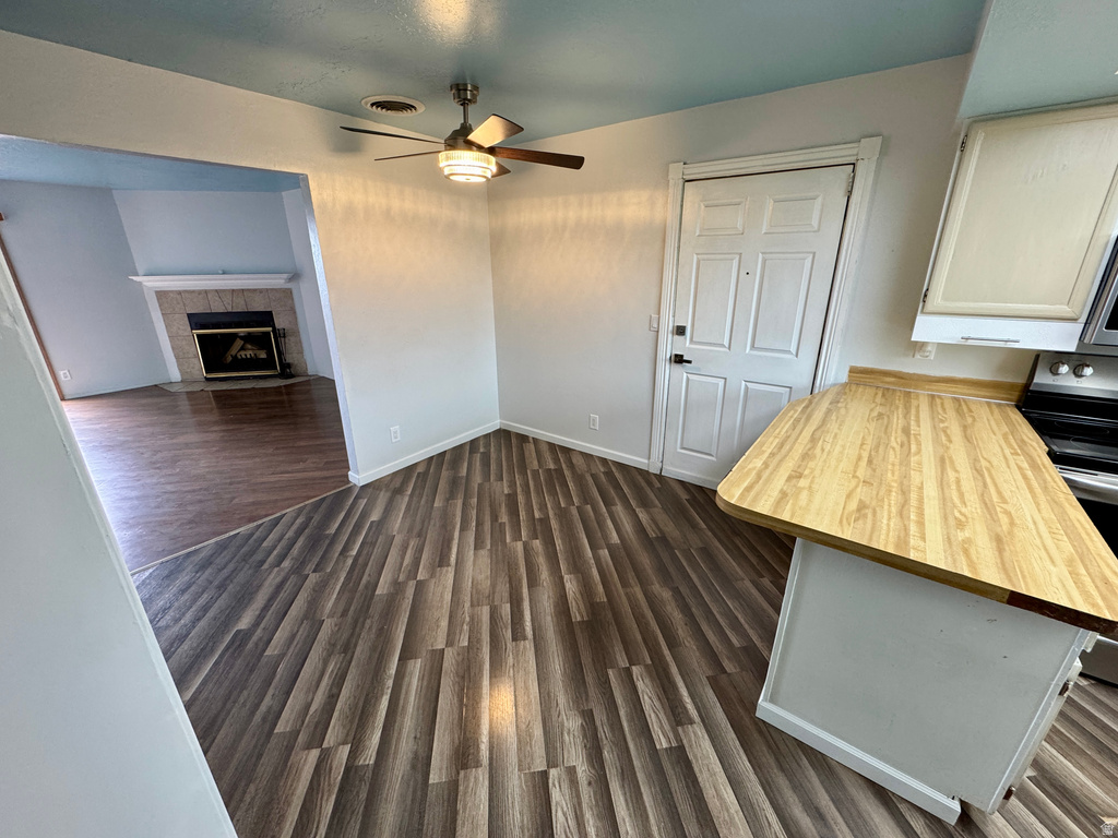 Unfurnished dining area with dark wood-type flooring, ceiling fan, and a fireplace