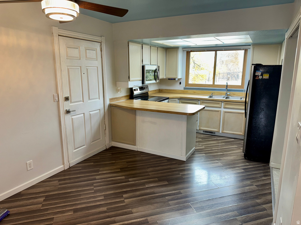 Kitchen with light countertops, appliances with stainless steel finishes, a peninsula, dark wood finished floors, and white cabinetry