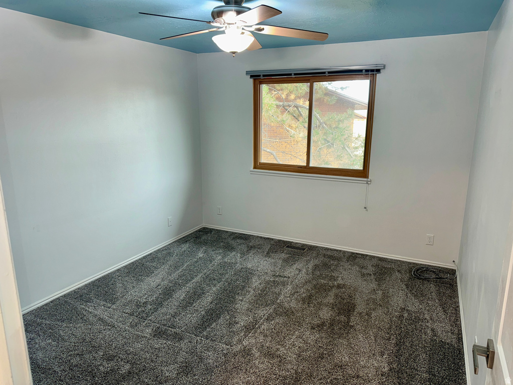 Empty room with dark colored carpet and ceiling fan