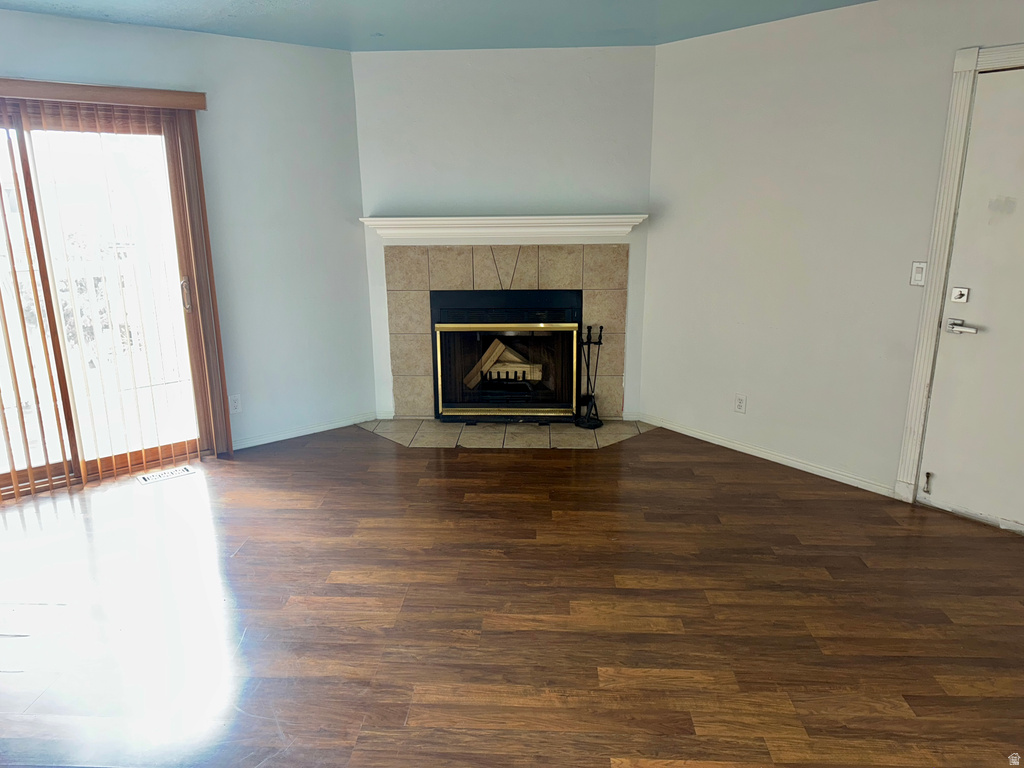 Unfurnished living room with dark wood-style flooring and a tiled fireplace