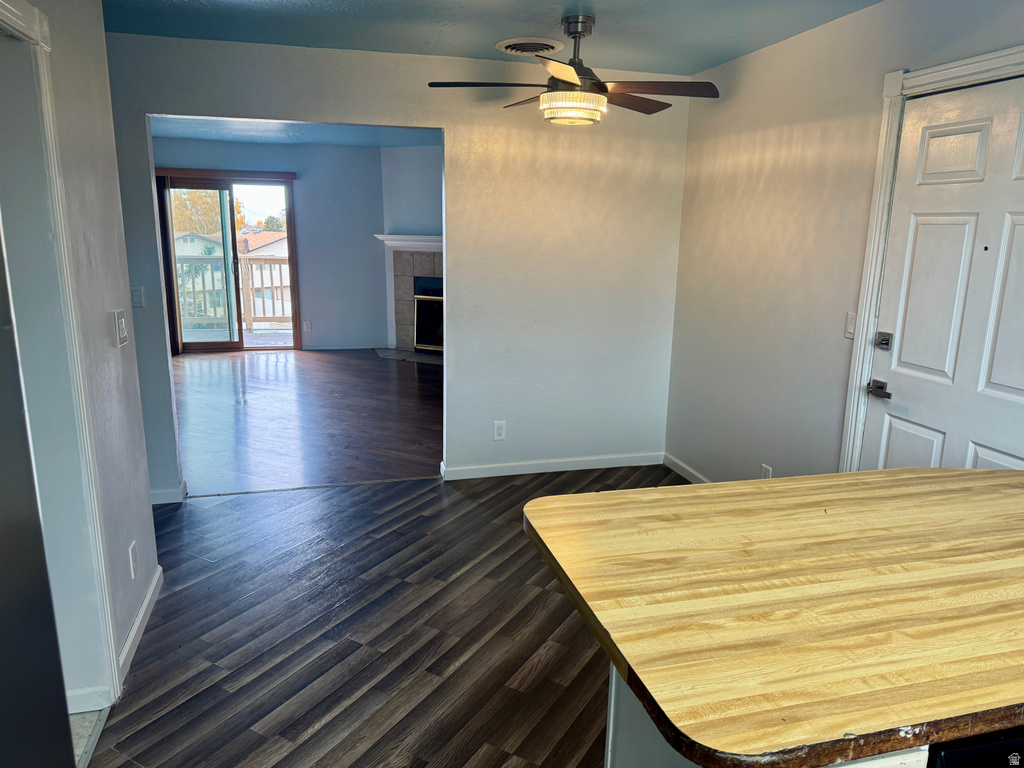 Unfurnished dining area with dark wood-style floors, ceiling fan, and a tiled fireplace
