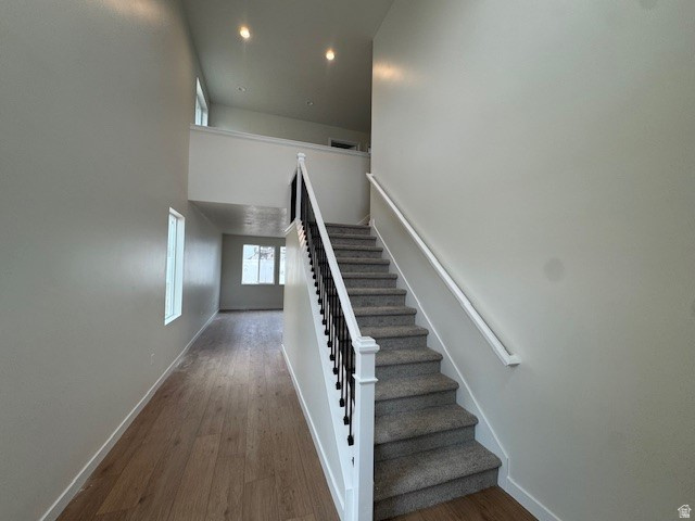 Staircase featuring a towering ceiling, wood finished floors, and recessed lighting