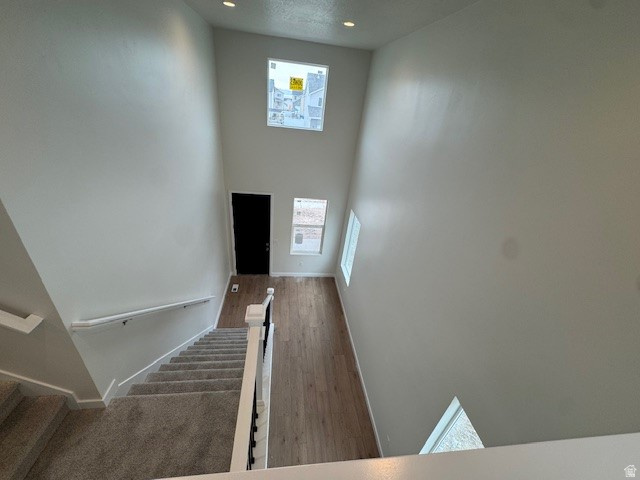 Staircase with a towering ceiling, plenty of natural light, wood finished floors, and recessed lighting