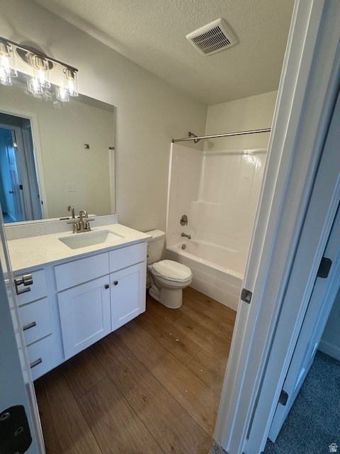 Bathroom featuring vanity, dark wood finished floors, a textured ceiling, and washtub / shower combination