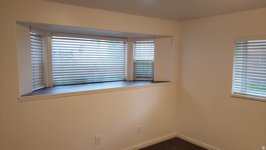 Unfurnished room featuring baseboards and dark carpet